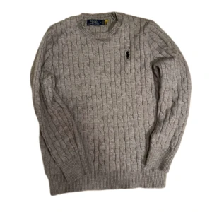 Polo Ralph Lauren kabelstickad tröja – grå, storlek M - Klassisk och tidlös kabelstickad tröja från Polo Ralph Lauren. Tillverkad i mjukt material med rund hals och ikoniskt broderad logga på bröstet. Perfekt för både vardag och mer uppklädda tillfällen – en riktig garderobsklassiker!  🧶 Material: Ullblandning (mjuk och värmande) 🎨 Färg: Ljusgrå 🎁 Skick: Bra skick – sparsamt använd, inga fläckar eller hål 🎯 Passform: Regular fit – bekväm och stilren 🐸 Hem: Rökfritt och djurfritt hem 💸 Pris: 450 [går o diskutera vid snabbaffär]  