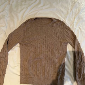 Beige kabelstickad tröja - Säljer en beige kabelstickad tröja med rund hals och långa ärmar. Tröjan har ett klassiskt flätmönster över hela och ribbade muddar vid ärmslut och nederkant. Perfekt för dig som gillar en chill och stilren look.