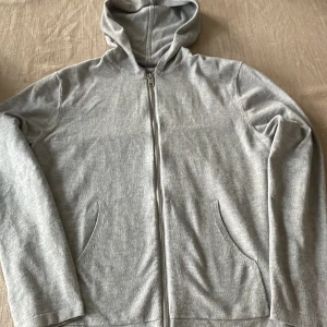 Grå zip up hoodie - En enkel och stilren grå hoodie med dragkedja framtill och två fickor. Tröjan har huva och långa ärmar, perfekt för chill dagar eller när du vill ha något bekvämt. Materialet känns mjukt och är troligtvis bomull eller polyester. Storlek S men passar även XS