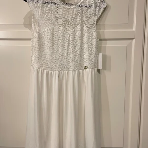 Vit spetsklänning  - Superfin vit kortklänning med spets upptill och v-ringning i ryggen. Kjolen är lätt utställd och klänningen har små ärmar. Perfekt för sommarens alla tillfällen! Materialet är mjukt och skönt, överdelen är i spets och kjolen i slätt tyg.