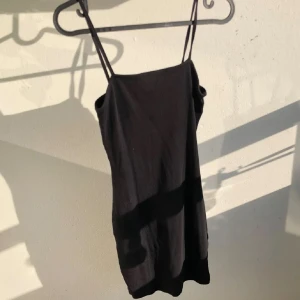 Svart ribbad kort klänning - En svart, tight ribbad klänning med smala axelband och rak halsringning. Klänningen är kort och har en enkel, basic design. Den är S men den passar XS S M då den är mycket stretch i