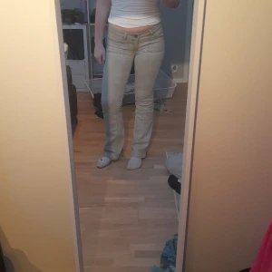 Grå bootcut jeans från NS Jeans - Snygga grå jeans från NS Jeans med bootcut passform och låg midja. Jeansen har breda framfickor och bakfickor med lock och knappdetaljer. Tillverkade i klassiskt jeanstyg som är mjukt och bekvämt. Perfekt för dig som gillar retrovibbar och coola detaljer.