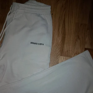 Vita mjukisbyxor från Arigato - Säljer ett par vita mjukisbyxor från Arigato med tryck 'ARIGATO ©2014' på ena benet. Byxorna har elastisk midja med snörning och raka ben. Perfekta för chill dagar och har en clean look som funkar till sneakers. Riktigt fina mjukis passar både tjej och kille  storlek M men ganska stora i storlek.
