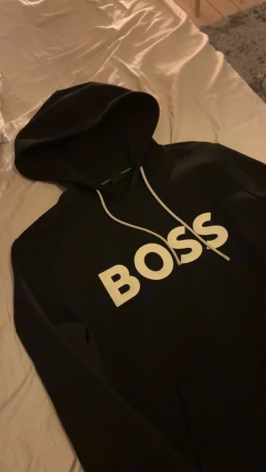 Svart hoodie från BOSS med tryck - Svart hoodie från Hugo boss med stor vit logga på bröstet. Riktig bra skick köpt på room 1006 i Malmö för 1800 använd fåtal gånger