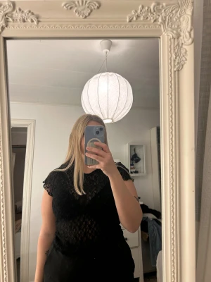 Svart spetsblus med kort ärm - Säljer en svart blus i spets med korta ärmar och rund hals. Blusen är genombruten med ett snyggt spetsmönster som ger en cool och feminin vibe. Perfekt att styla med jeans eller kjol för en trendig look.