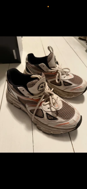 Axel Arigato mesh sneakers vit/orange - Säljer ett par chunky sneakers från Axel Arigato med vit och orange mesh, svarta och grå detaljer samt snörning. Skorna har en sportig vibe med tjock sula och coola kontraster. Axel Arigato-logga på plösen och insidan. Perfekta för dig som gillar streetstyle.