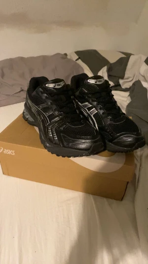 Svarta sneakers med silvriga detaljer - Säljer ett par svarta sneakers med silvriga detaljer. Skorna har snörning, platt sula och rund tå. Ovandelen är i mesh och syntet för bra ventilation och komfort. Perfekt för dig som gillar sportig stil och vill ha bekväma skor.