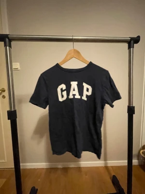 Mörkblå GAP t-shirt med tryck - Snygg mörkblå t-shirt från GAP med klassiskt vitt logotryck framtill. T-shirten har rund halsringning och korta ärmar. Tillverkad i mjuk bomull som är skön att ha på sig hela dagen.