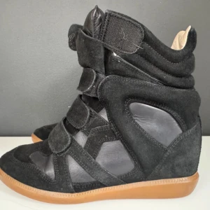 Svarta wedge sneakers med kardborre - Säljer ett par svarta Isabel Marant Bekett wedge sneakers. Skorna har en mix av mocka och skinn och är i modellen BEKETT, högre skaft och brun gummisula. De är använda vid runt 7 tillfällen och är som nya, inga yttre defekter, men det finns tecken på användning inuti skon på sulan!!! Nypris är 6500kr men säljer för mindre än halva priset då de aldrig kommer till användning!!💕KOM GÄRNA MED BUD! 