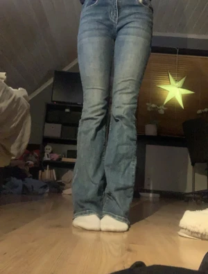 Blå bootcut jeans med hög midja - Snygga blå jeans med bootcut passform och hög midja. Klassisk femficksmodell med dragkedja och knapp framtill. Jeansen har en lätt tvättad look och är tillverkade i jeansmaterial som sitter bekvämt. Perfekta för dig som gillar retrovibbar och vill ha ett par jeans med lite extra sväng i benen.