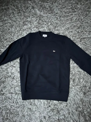 Mörkblå sweatshirt från Woolrich - Snygg mörkblå sweatshirt från Woolrich med rund hals och ett litet broderat får på bröstet. Tröjan är i classic fit och den har aldrig använts.