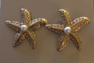 Guldiga örhängen strass med pärlor - Unika örhängen formade som  i guld med glittrande stenar och en vit pärla i mitten. Perfekt för dig som vill sticka ut med ett coolt och annorlunda smycke. Passar till alla som gillar havsinspirerad design och bling.