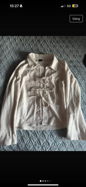 Vit knyt-skjorta med snören - Vit skjorta från Monki i storlek L, med  snörning framtill och klassisk krage. Materialet är mjukt och har en lätt struktur. Skjortan är långärmad och har en omlott-design.