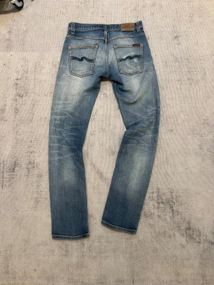 Nudie jeans grim Tim - Snygga blå jeans från Nudie Jeans med klassisk femficksdesign och coola slitningar på både fram- och baksida. Modellen är Grim Timm passform.