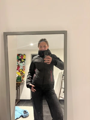 Svart Everest skidjacka - Svart skidjacka från Everest med rosa dragkedja och detaljer. Jackan är vattentät med TCS Waterproof-system och har flera praktiska fickor, både invändigt och utvändigt. Hög krage och långärmad modell. Snygg och funktionell design.