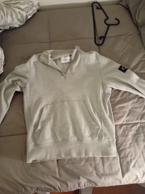 Grå half zip tröja Calvin Klein Jeans - Snygg grå tröja från Calvin Klein Jeans med half zip framtill och stor CK-logga på ärmen. Tröjan har en ribbad struktur, lång ärm och en praktisk magficka. Perfekt för dig som gillar stilren och enkel design.                                                            Ny priss 700 kr,skick 8/10.