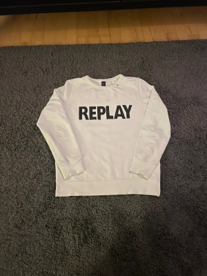 Vit sweatshirt från Replay - Säljer en stilren vit sweatshirt från Replay med svart REPLAY-tryck på bröstet. Tröjan har rund halsringning, långa ärmar och ribbade muddar. Perfekt för en clean och avslappnad look. Passar dig som är emellan 12-14