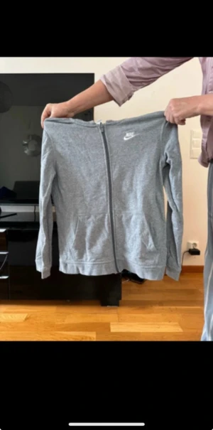 Grå zip hoodie från Nike - Säljer en grå hoodie från Nike med dragkedja framtill och klassisk logga på bröstet. Tröjan har långa ärmar, två fickor och är tillverkad i mjuk bomullsmix. Perfekt för chill eller träning, enkel och stilren design.