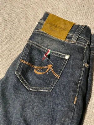 Jacob Cohen mörkblå jeans straight fit - Jacob Cohen jeans i mörkblå tvätt med klassisk straight fit. Snygga kontrastsömmar och unik broderad detalj på bakfickan. Lyxig patch i mocka baktill och insida med exklusiva etiketter. Perfekt för dig som gillar premium denim och stilrena detaljer.