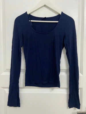 Mörkblå långärmad topp med slits - Säljer en mörkblå långärmad topp med rundad halsringning och slits vid armen. Materialet känns mjukt och stretchigt. Perfekt för dig som gillar minimalistisk stil. Det finns en jätte liten vit fläck på tröjan men den går bort när man tvättar den (jag kommer göra det innan jag skickar). 