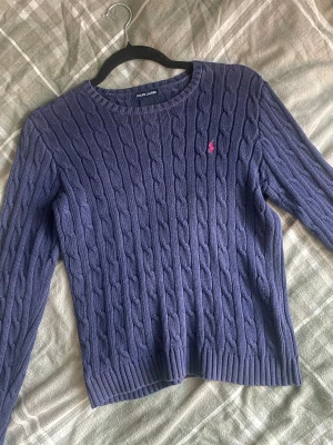 Kabelstickad Ralph Lauren - Superfin kabelstickad mörkblå tröja från Ralph Lauren. Lappen med storlek är bortklippt, men  skulle säga att den passar XXS-S. Rosa broderad häst på bröstet. 100% cotton