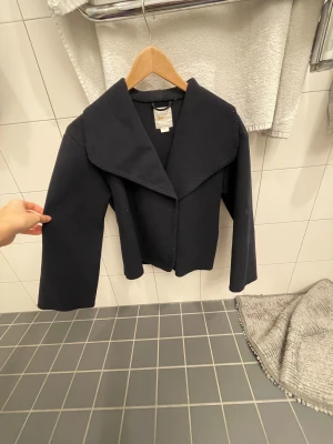 Svart kavaj med bred krage - Snygg svart kavaj med bred krage och raka, långärmade ärmar. Jackan har en stilren och minimalistisk design som passar perfekt till en cool och dressad look. Materialet känns mjukt och har en lätt struktur, vilket gör den bekväm att bära.