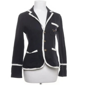 Svart kofta från Ralph Lauren  - Svart kofta från Ralph Lauren med vit kontrastkant och klassisk krage. Jackan har tre knappar framtill, fickor med vit kant och dekorativa knappar vid ärmslut. Materialet är stickat och ger en mjuk känsla 