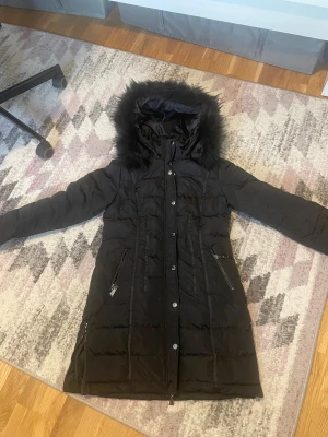 Svart lång dunjacka Chiara Forthi - Säljer en helt ny svart vinterjacka Jag säljer denna snygga och varma vinterjacka som är helt oanvänd. Den har bara hängt i garderoben eftersom jag redan har en annan jacka. Nypriset ligger runt 2 300 kr, och jag säljer den nu för 1 100 kr. Det är en tjock och riktigt varm modell med luva och fin fuskpälskant. Jag är 162 cm lång och både längden och storleken sitter perfekt på mig. Jackan är helt ny, fräsch och i toppskick – ett riktigt bra kap för den som vill ha en pålitlig vinterjacka.