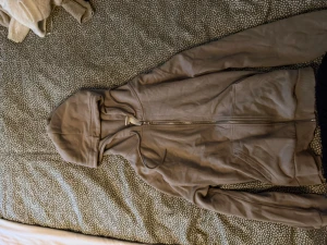 Beige hoodie med dragkedja från H&M - Säljer en beige hoodie från H&M med dragkedja framtill och huva med snörning. Tröjan har långa ärmar, ribbade muddar och är tillverkad i mjuk bomullsmix. Perfekt för en chill och avslappnad stil.