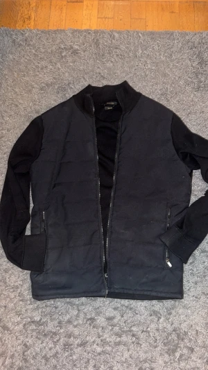 Svart lätt jacka från Massimo Dutti - Svart lätt jacka från Massimo Dutti med ribbad krage och muddar. Jackan har två sidofickor och en stilren, quiltad framsida.