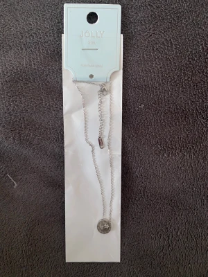 halsband - rostfritt stål - Snyggt halsband från JOLLY i rostfritt stål med en tunn silverfärgad kedja och ett runt hänge som liknar en klocka med romerska siffror. Perfekt accessoar för dig som gillar stilrena detaljer med en twist. Helt ny i förpackning🥰