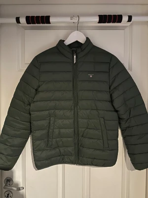 Grön pufferjacka från GANT - Tunn grön dunjacka från gant i storlek 158/164.         Har en liten defekt på ryggen.