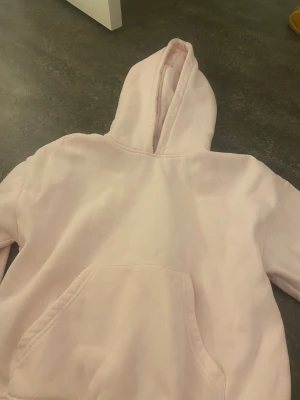 Ljusrosa hoodie med huva - Mysig ljusrosa hoodie med stor ficka framtill och ribbade muddar vid ärmslut och nederkant. Tröjan har en klassisk huva och är tillverkad i mjuk bomullsmix, perfekt för chill dagar. Enkel och stilren design utan tryck eller mönster. Har aldrig använt den här från Gina lite stor storleken