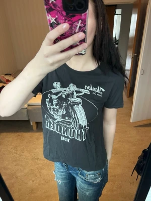 Svart t-shirt med motorcykeltryck - Cool svart t-shirt med stort vitt tryck av en motorcykel och texten 'Thunder 1972' framtill. Klassisk rund hals och korta ärmar. Perfekt för dig som gillar streetstyle och vill sticka ut med en edgy vibe.