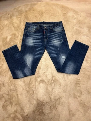 Disquared 2 blå jeans med slitningar - Säljer ett par Disquared 2jeans i mörkblå tvätt med snygga slitningar och ljusa partier. Klassisk femficksmodell med raka ben och normal passform. Tillverkade i tåligt jeanstyg med en cool vintagekänsla. Perfekta för dig som gillar en avslappnad men stilren look. Kom dm för eventuella frågor 🧐pris kan diskuteras 😇💯