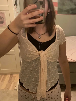 Ljusrosa blommig blus med knyt - Säljer en superfin ljusrosa blus i transparent material med blommigt mönster. Toppen har korta ärmar och en stor knytning framtill som ger en söt och trendig look. Perfekt att styla över ett linne eller topp. Materialet är lätt och luftigt.