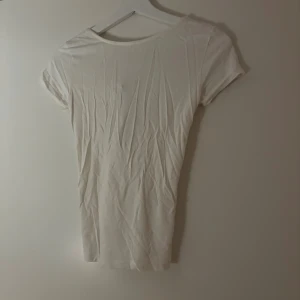 Vit topp med knyt i ryggen - Säljer en enkel och stilren vit topp med korta ärmar och rund hals. Toppen har en snygg detalj med knyt i ryggen som ger en extra touch. Tillverkad i mjuk bomull, perfekt till sommaren eller våren. Den är i storlek Xs eller S och den är från Lager 157. Pris kan diskuteras vid snabb affär