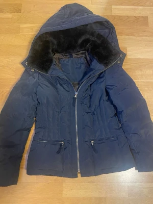 Mörkblå jacka från Zara - Säljer en mörkblå pufferjacka från Zara med huva och mjukt foder i kragen. Jackan har dragkedja, men på den är den lite rostig men absolut inget som syns tydligt! Därav priset.