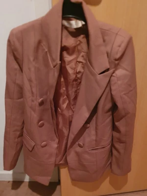 Kavaj - Säljer en brun kavaj med breda slag och dubbelknäppning framtill. Kavajen har två fickor med lock och är helfodrad. Perfekt för dig som vill ha en klassisk men trendig look. Passar till många olika outfits och har en snygg, rak passform.