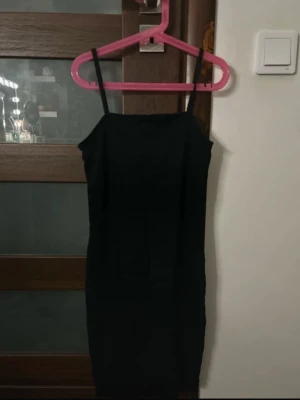 Svart tight klänning från Amisu - Säljer en svart, tight klänning från Amisu med smala axelband och rak halsringning. Klänningen är kort och har en enkel, stilren design som sitter snyggt på kroppen. Perfekt för dig som gillar minimalistisk stil.