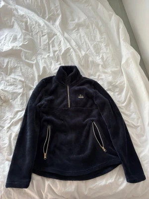 Mörkblå varma ridtröja  - Supermjuk mörkblå fleece med half zip och två fickor med dragkedja.Perfekt att ha i stallet en kall dag. Storlek är 158-164 