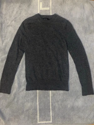 Mörkgrå merinoullströja från Riley - Säljer en stilren mörkgrå tröja från Riley i mjuk merinoull. Tröjan har rund halsringning och långa ärmar, perfekt för lager-på-lager under kyliga dagar. Enkel och klassisk design som funkar till allt.