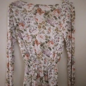 HELT NY OANVÄND vit och blommig omlott topp från Bik Bok, Small - Helt ny oanvänd supersöt omlott-topp från Bik Bok med blommigt mönster i pastelliga toner av tex rosa,  lila och, grön. Toppen har v-ringning, långa ärmar och markerad midja. Perfekt för vår och sommar, i mjukt och lätt material. Storlek Small. Felfri.