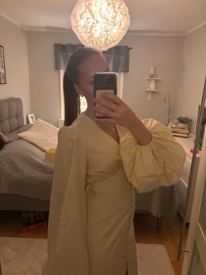Randig långklänning från Adoore - Säljer en Positano Maxi Dress från Adoore i ljusgul och med smala ränder. Klänningen har v-ringning, knappar framtill och puffiga långärmar med resår vid ärmslut. Aldrig använd och med prislapp kvar💕🌼