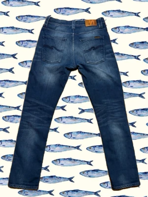 Blå Nudie Jeans grim tim - Säljer ett par blå Nudie Jeans Skinny Lin med klassisk femficksdesign och signaturbroderi på bakfickorna. Jeansen har en skinny passform, normal midja och är tillverkade i stretchig bomullsdenim för extra komfort. Perfekta för dig som gillar en smal siluett.
