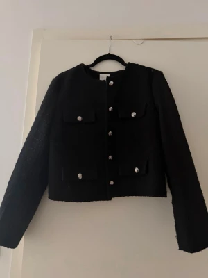 Svart kofta med silvriga knappar - Stilren svart kofta i grovstickat material med raka axlar och långa ärmar. 