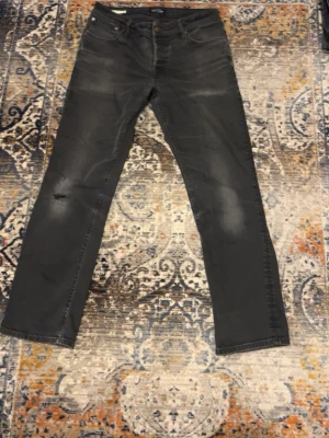 Svarta jeansbyxor i rak modell - Svarta jeansbyxor med lätt slitning och klassiska fem fickor. Byxorna har rak passform och subtila detaljer på bakfickorna. Perfekta för en avslappnad stil och passar till det mesta.