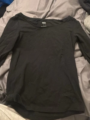 Svart långärmad topp från 157 - En enkel svart långärmad topp från 157 i mjuk bomullsblandning med lite stretch. Modellen har rundad halsringning och sitter snyggt mot kroppen. Perfekt att styla med jeans eller kjol för en clean look.