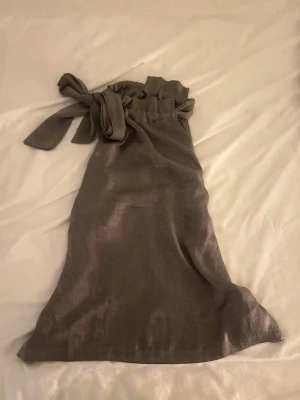 Brun halterneck  från Bubbleroom - Säljer en brun halterneck från Bubbleroom x Moa Mattsson i storlek 36. Toppen är ärmlös och har en snygg knytning vid halsen. Materialet känns mjukt och har ett lätt glansigt utseende, rosetten går att få så att den är på ryggen istället om man vill💗