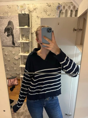 Mörkblå randig stickad tröja - Säljer en mörkblå stickad tröja med vita horisontella ränder och krage. Tröjan har en avslappnad passform och långa ärmar. Snygg till både jeans och kjol! Säljer då det inte kommer till användning längre. Passar mig som brukar ha s/m